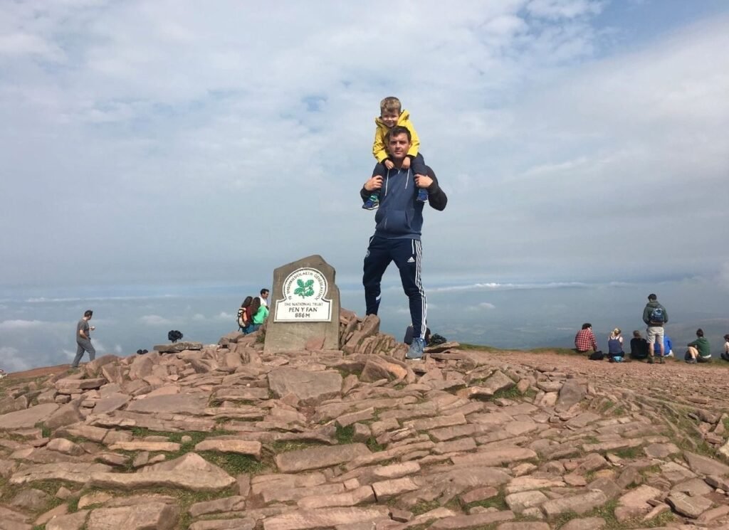 Man on a mountain peak with his son on his shoulders- time saving workouts with the family