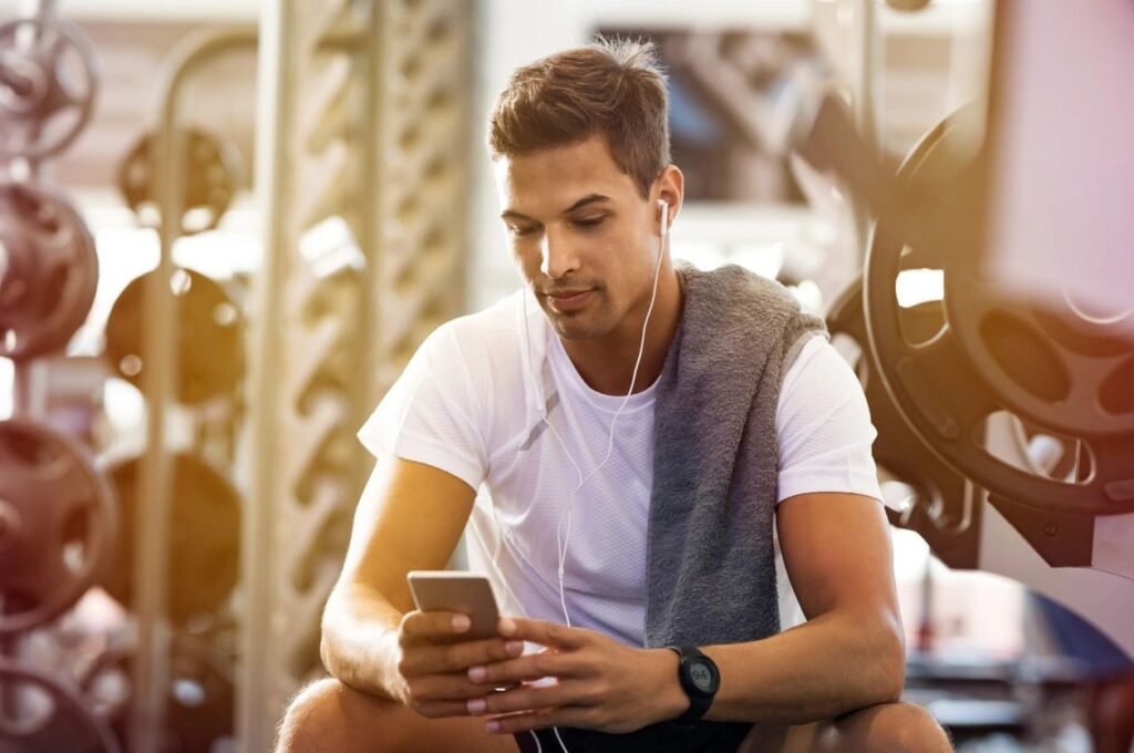 Young male gym goer reading his mobile phone in-between sets