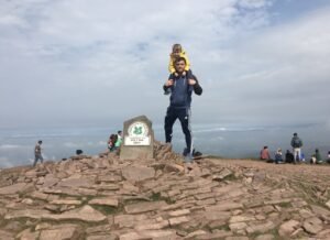 “Dad with son on shoulders at mountain peak – fitness and family balance for dads over 40”