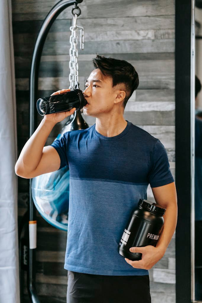 Athletic man hydrating with protein shake during workout in gym.