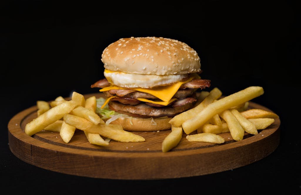 Close-up of a mouthwatering cheeseburger with fries on a dark background.