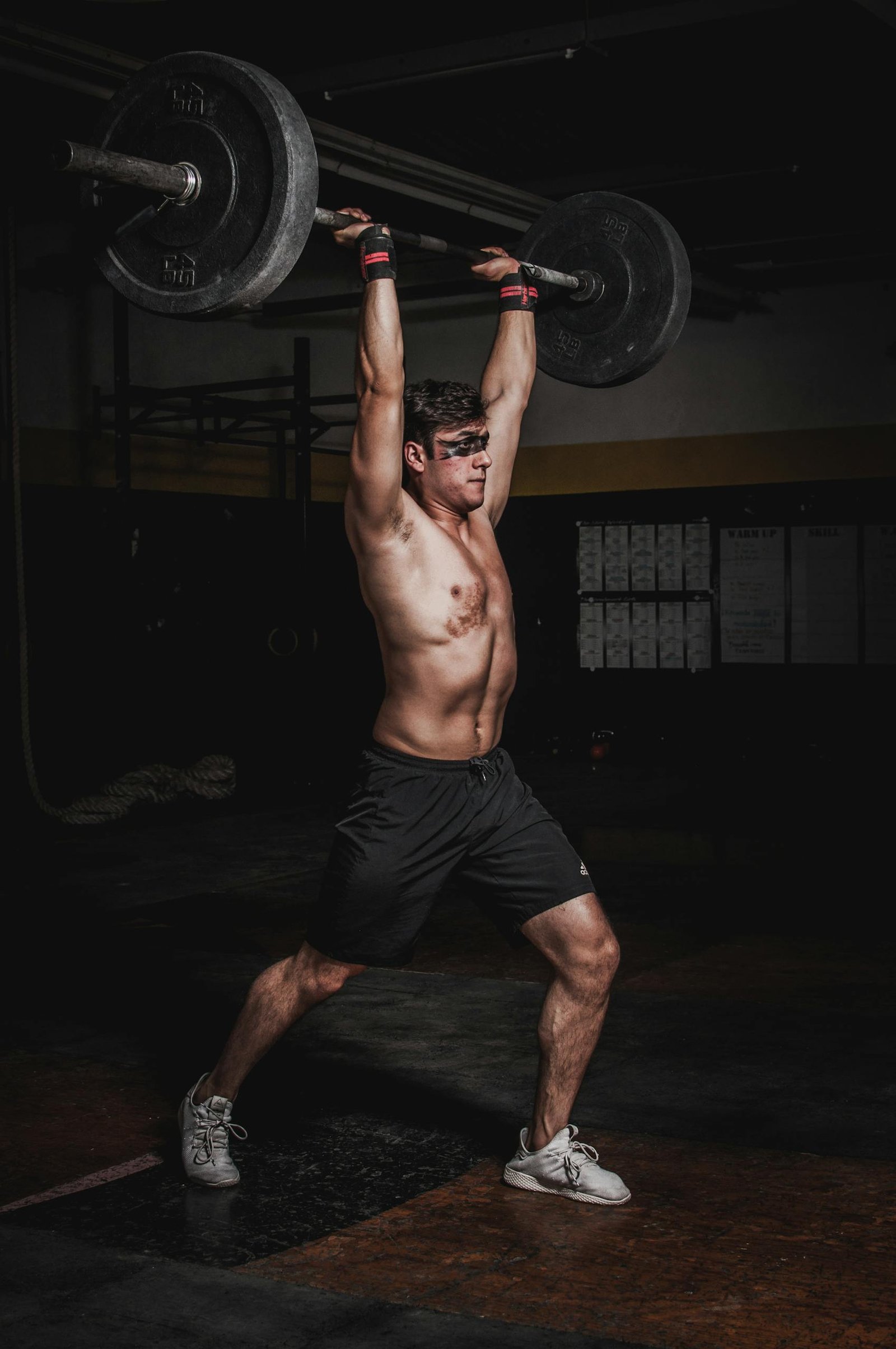 Shirtless man demonstrating strength and fitness by lifting a heavy barbell indoors.