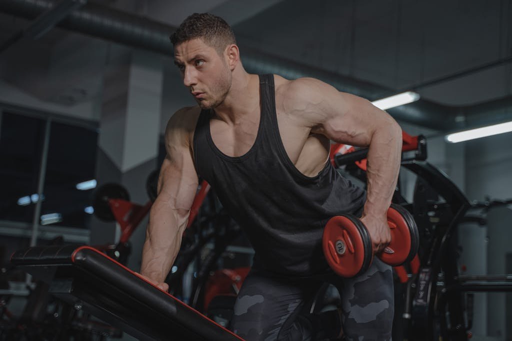 Strong male bodybuilder lifting dumbbells in a gym environment.